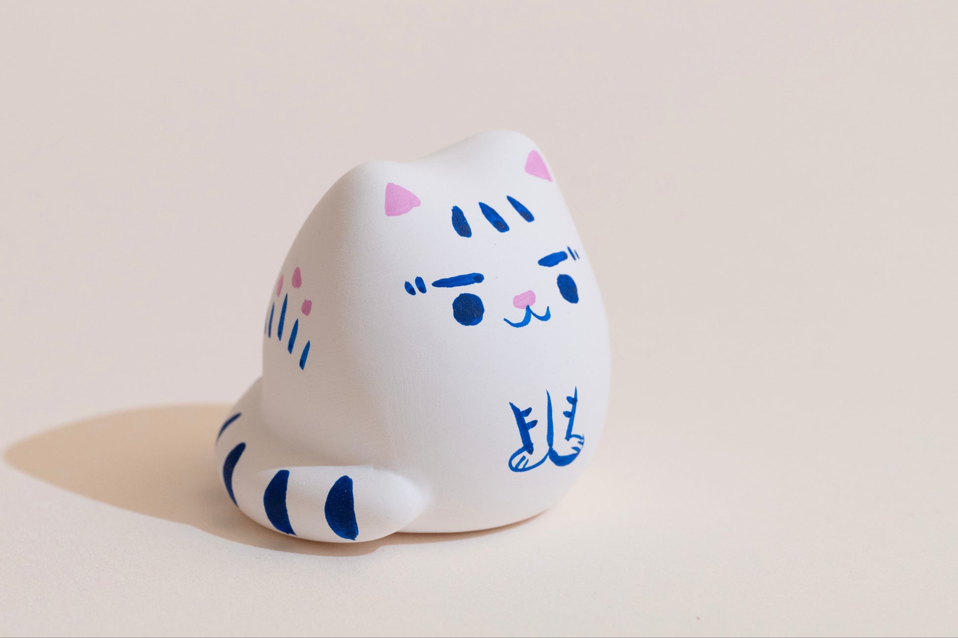 White cat-shaped figurine with blue accents on a beige background
