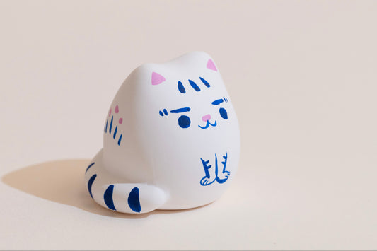 White cat-shaped figurine with blue accents on a beige background